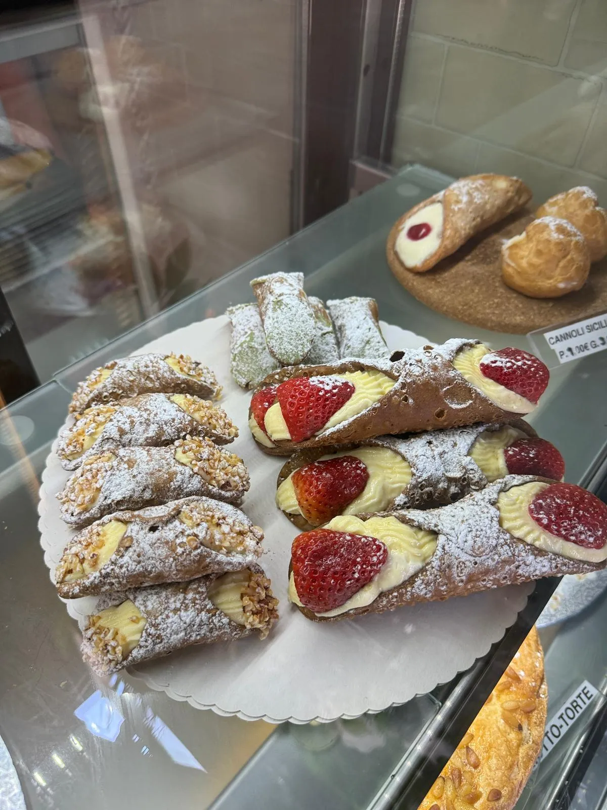 Vitrine mit sizilianischen Cannoli, Erdbeer-Cannoli und pistaziengekröntem Gebäck