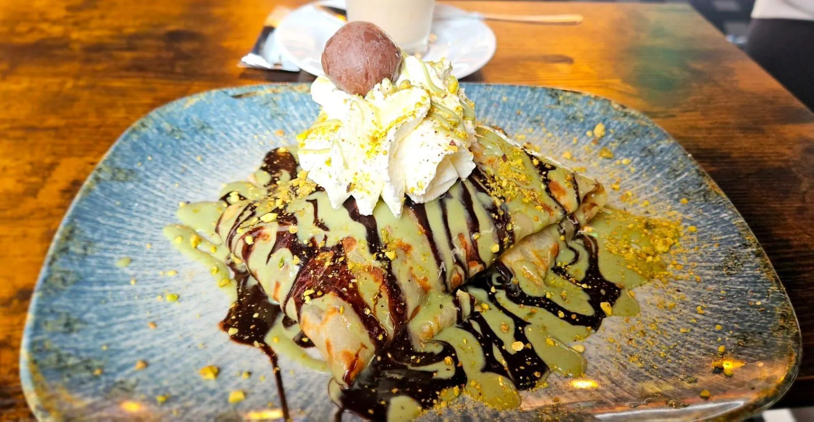 Gefalteter Crêpe mit Schokoladen- und Pistaziensauce und einer Praline auf blau gemustertem Teller