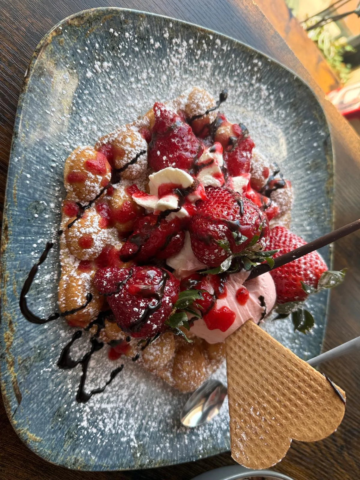 Bubble Waffel mit Erdbeeren, rosa Eis und Puderzucker auf rustikalem Teller