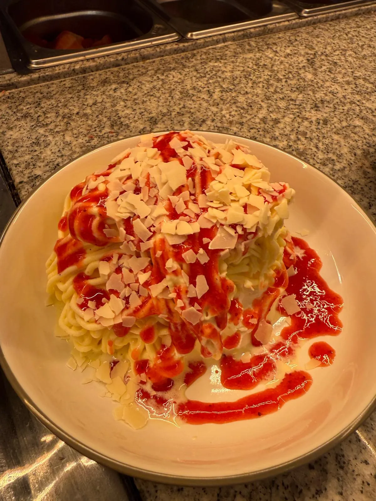 Spaghettieis mit Erdbeersauce und weißer Schokolade auf weißem Teller